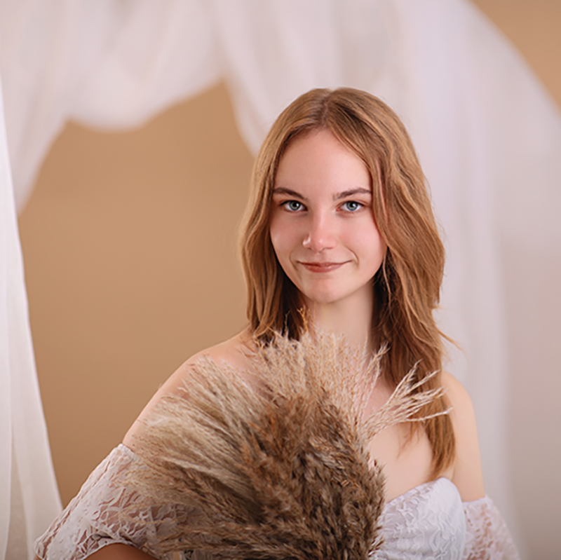 Portrait einer jungen Frau in einem weißen Kleid aus Spitze im Fotostudio mit einem Stoff Ring im Hintergrund